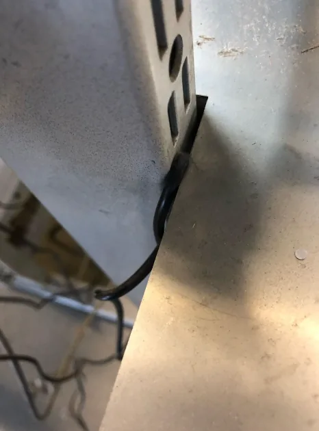 Kabel geklemd achter een metalen kast